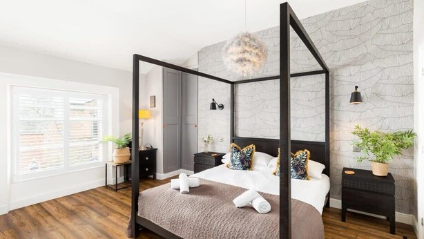 Ein modernes Schlafzimmer mit einem Himmelbett, einer Wand im Marmor-Look und einem großen Fenster mit Jalousien.