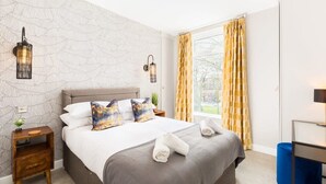 Ein Hotelzimmer mit einem großen Bett, zwei Nachttischen, einem Fenster mit Vorhängen und Wandleuchten.