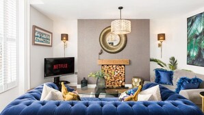 Ein Wohnzimmer mit blauem Sofa, Kamin, Fernseher und einem großen Gemälde.