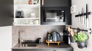 A modern kitchen with a built-in microwave, a coffee maker, and a kettle on the countertop. There are utensils hanging on the wall and a small plant on a hook. - Second floor compact studio with mini kitchen (Warrington)