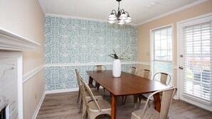 Ein Esszimmer mit Holztisch und -stühlen, einer Vase auf dem Tisch und Wandpapier mit Muster.