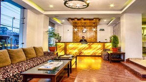 A hotel lobby with a reception desk, a sofa, a coffee table, and a staircase leading to the upper floor. - MeroStay 187 Hotel KM (Kathmandu)