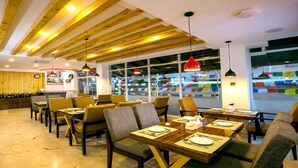 A restaurant with wooden ceiling beams, tables set for dining, and a view of colorful flags outside. - MeroStay 187 Hotel KM (Kathmandu)