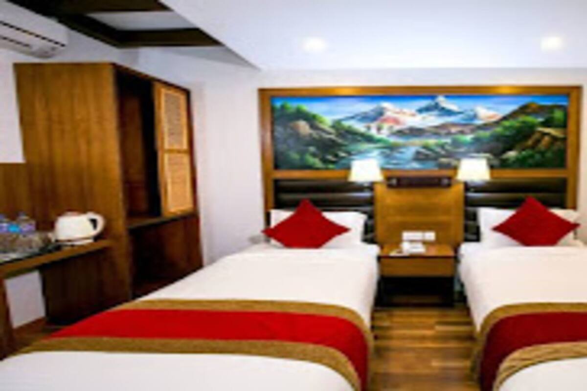 Een hotelkamer met twee bedden, een schilderij van een bergachtig landschap, een houten hoofdbord en een nachtkastje met een lamp.