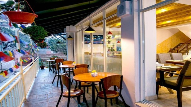 An outdoor seating area with tables and chairs, a wooden ceiling, and hanging plants. - MeroStay 187 Hotel KM (Kathmandu)