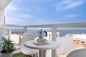 A balcony with a white table, two white chairs, a potted plant, and a view of the sea. - Vacation Apartment 'Alcamar' with Sea View, Balcony and Wi-Fi (Alcalá)