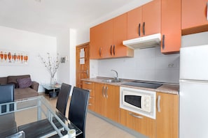 A modern kitchen with wooden cabinets, a built-in oven, and a dining area with a glass table and chairs. - Vacation Apartment 'Alcamar' with Sea View, Balcony and Wi-Fi (Alcalá)