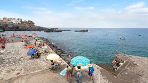 Une plage avec des parasols, des gens et une côte rocheuse.