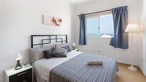 Une chambre à coucher avec un lit, une table de chevet, une lampe et une fenêtre avec des rideaux.