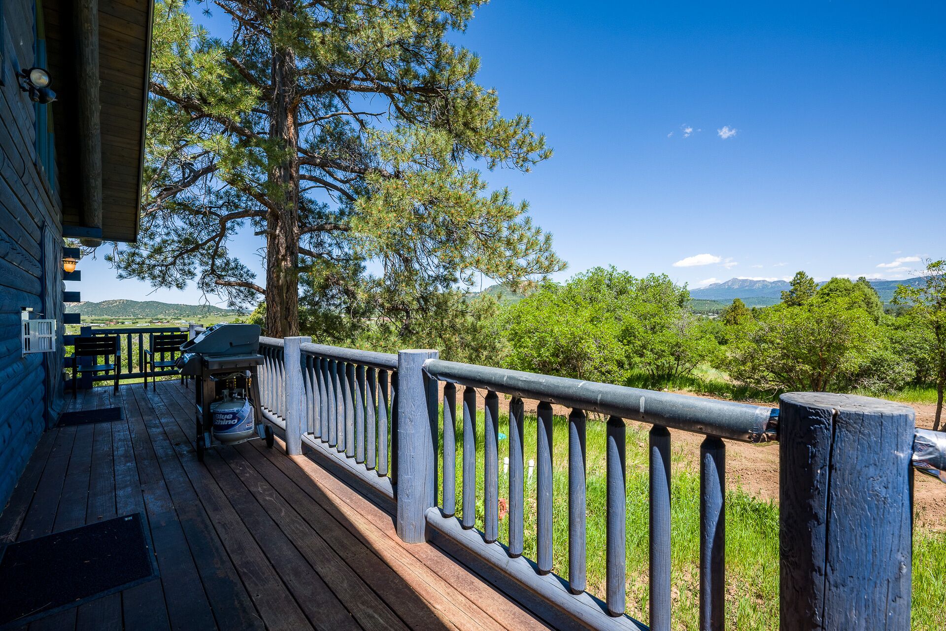 A wooden deck with a railing, a grill, and a view of a forest and mountains.