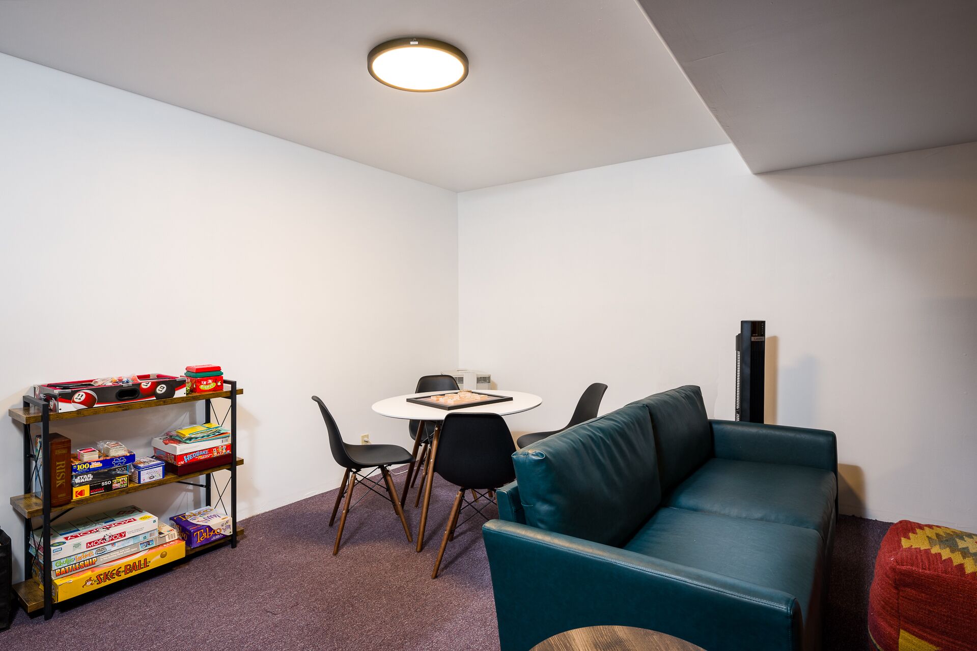 A small, modern room with a teal sofa, a coffee table, and a bookshelf filled with board games.