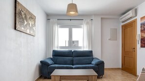 Ett rum med en blå soffa, ett träbord, ett konstverk i form av en jordglob, ett fönster med gardiner och en dörr.