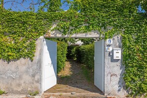 Ein gepflasterter Weg führt durch ein Rundbogenportal mit efeuüberwachsenen Mauern und einem Schild mit der Nummer 73.