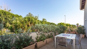 Eine Terrasse mit Tisch und Stühlen, umgeben von Topfpflanzen und Blick ins Grüne.