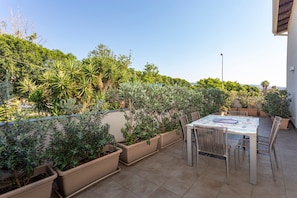 A patio with a table and chairs, surrounded by potted plants and a view of greenery.