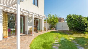 Ein modernes Haus mit einer Steinterrasse, einem überdachten Außenbereich und einem gepflegten Rasen.