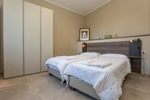 Ein Schlafzimmer mit einem Bett, Nachttischen, einem Kleiderschrank, einem Regal mit Büchern und einem Bild sowie einer Wandlampe.
