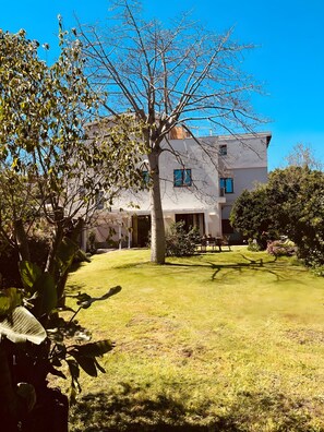 A two-story building with a well-maintained lawn and a large tree in the foreground. - Holiday Apartment 'A Casa Nostra' with Terrace, Shared Garden and Wi-Fi (Catania)