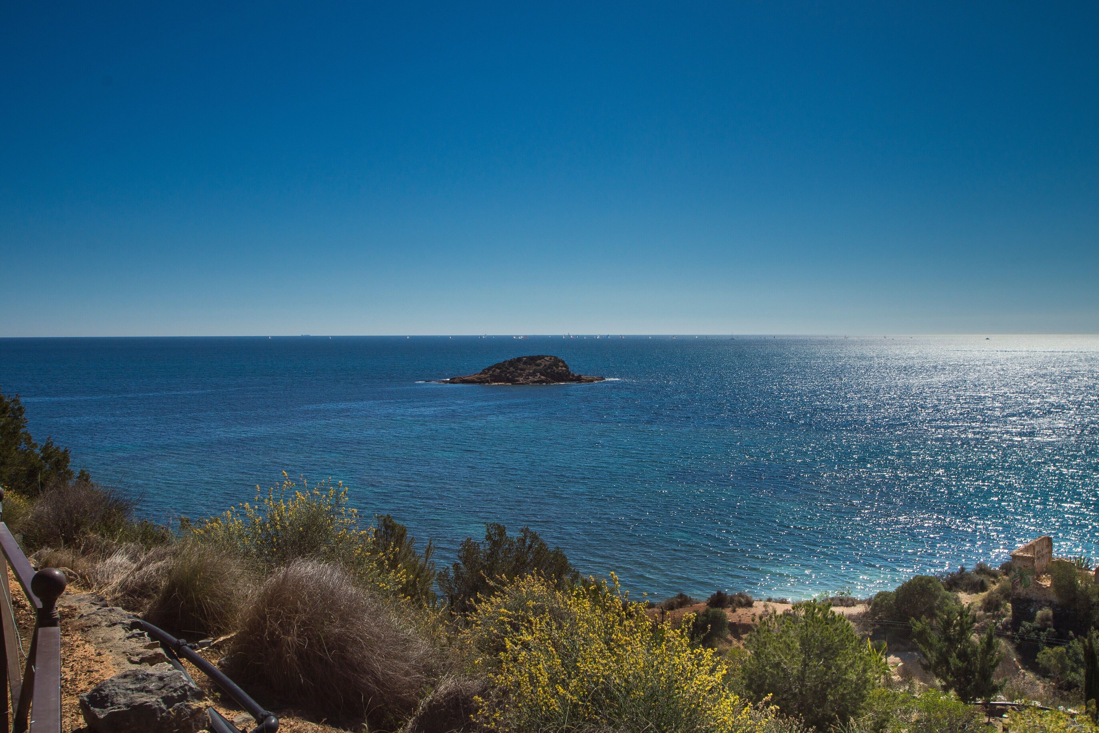 A coastal landscape with a clear view of the sea, a rocky outcrop, and sparse vegetation.