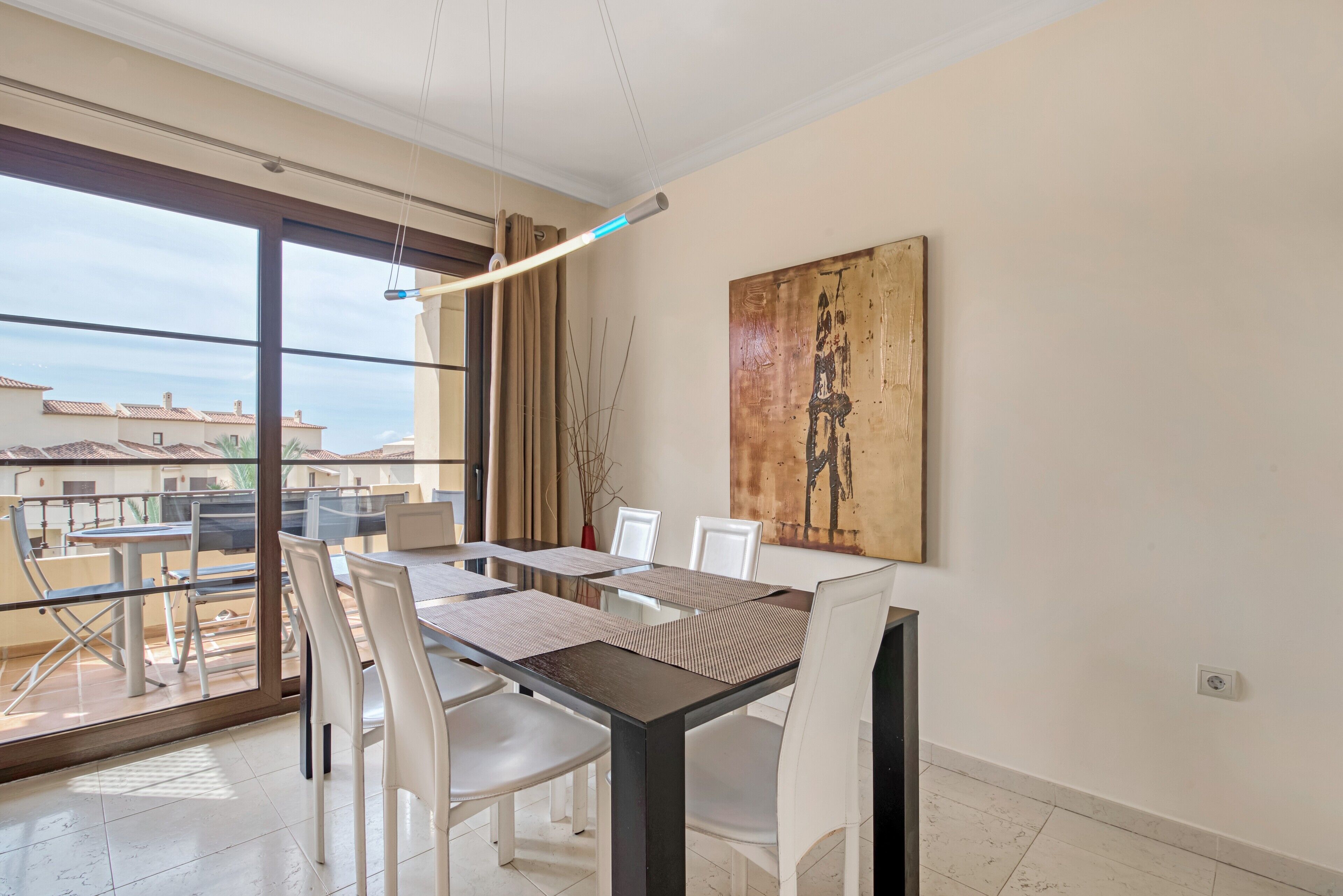 Un espace repas moderne avec une cloison en verre, des chaises blanches, une table sombre et un grand tableau abstrait accroché au mur.