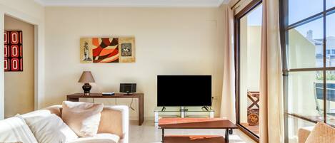 A living room with a sofa, a coffee table, a flat-screen TV, and artwork on the wall.