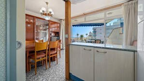 A compact kitchen with wooden cabinets, a dining area with chairs, a ceiling light fixture, and a view of the outside. - Apartment 'Edificio Victoria 1º-1ª' with Sea View, Private Terrace and Wi-Fi (Sant Salvador (El Vendrell))