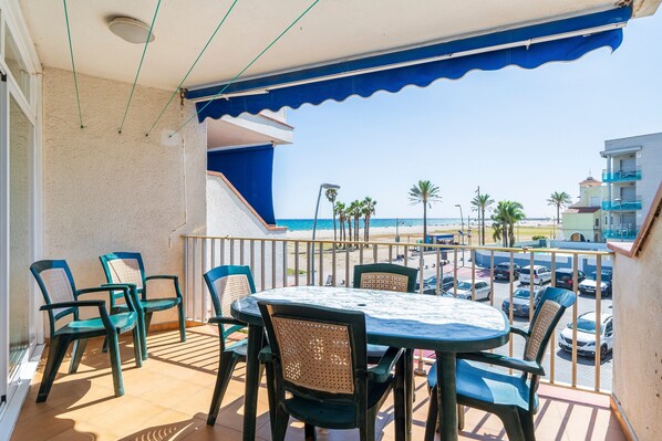 Ein Balkon mit Tisch und Stühlen, mit Blick auf Strand und Parkplatz.