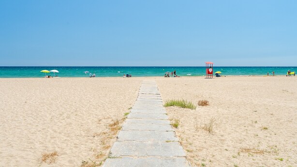 Ein Strand mit einem klaren Weg zum Wasser, einem Rettungsturm und Sonnenschirmen.