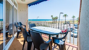 Ein Balkon mit Tisch und Stühlen, Blick auf den Strand und geparkte Autos.