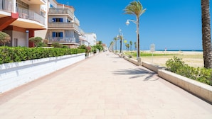 Eine Uferpromenade mit mehrstöckigen Gebäuden, einem wolkenlosen Himmel und einem Strand in der Ferne.