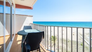 Ein Balkon mit Tisch und Stühlen, der Blick auf einen Strand mit blauem Himmel bietet.