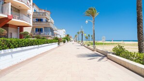Eine Uferpromenade mit mehrstöckigen Gebäuden, einem von Palmen gesäumten Weg und einem Strand im Hintergrund.