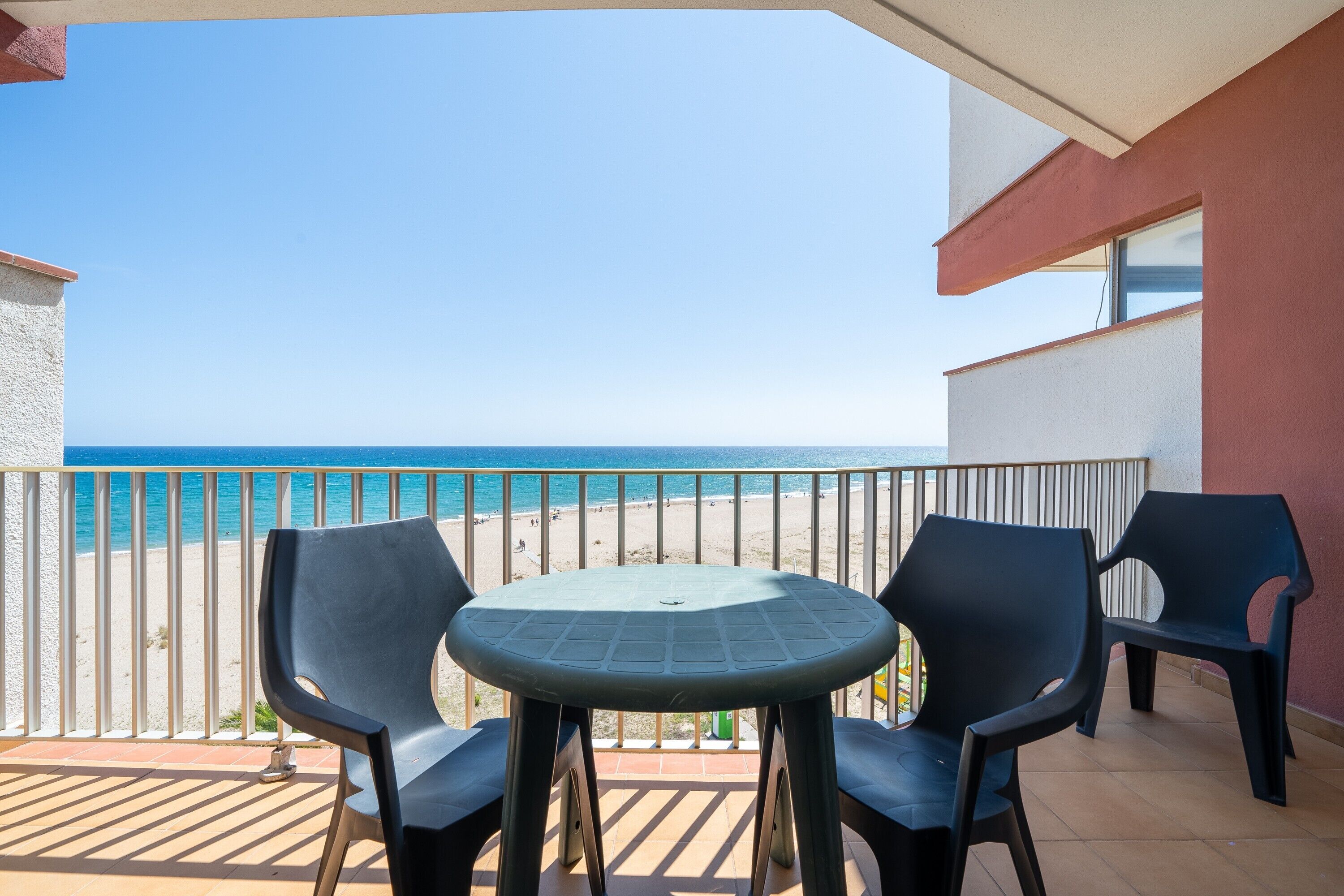 A balcony with a table and chairs, overlooking a beach.