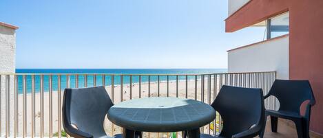A balcony with a table and chairs, overlooking a beach.