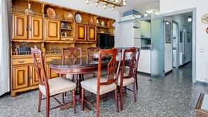 Ein Essbereich mit einem runden Tisch und Stühlen, einer Holzkommode mit Dekorationsobjekten und einer Küche im Hintergrund.