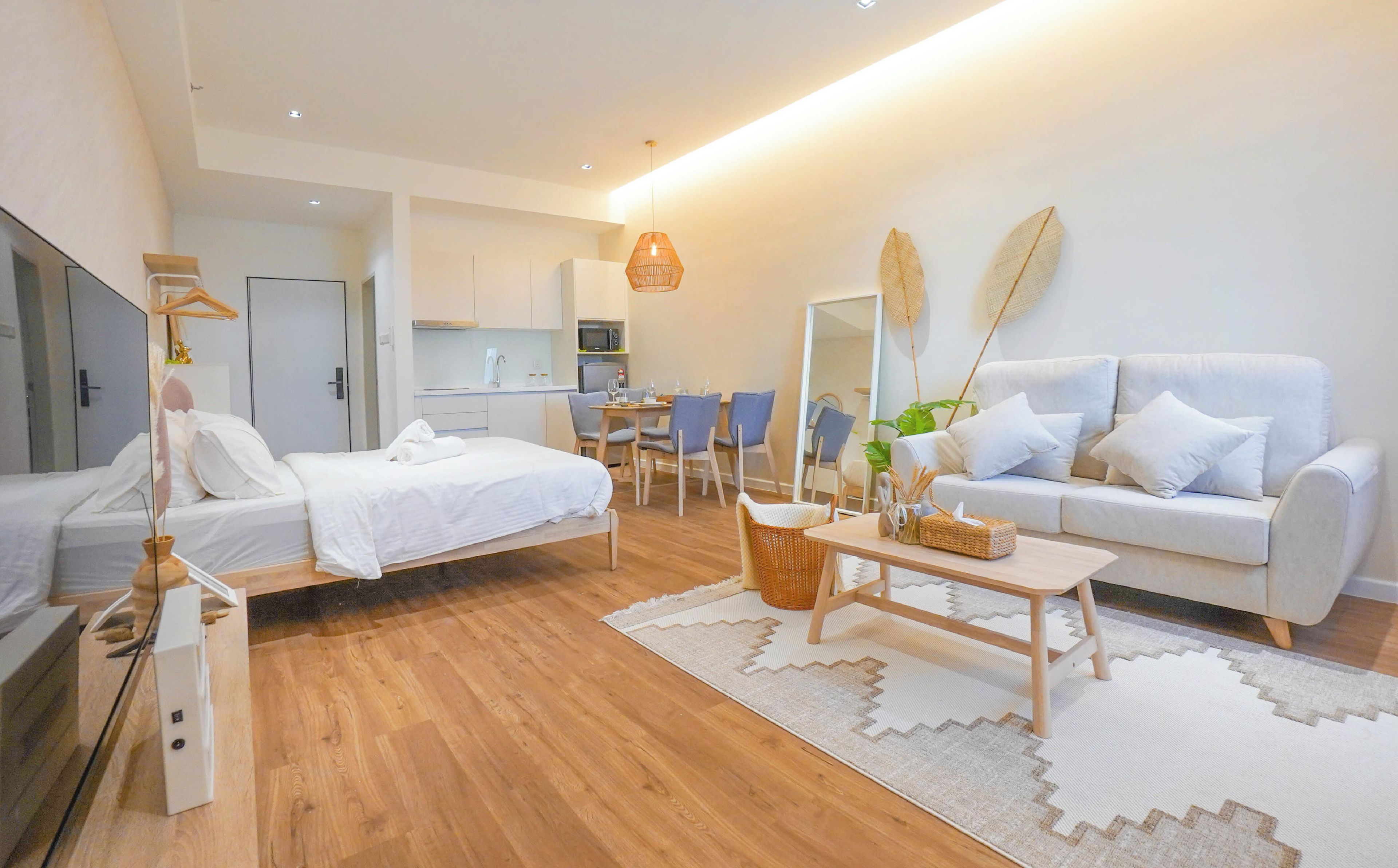 Una habitación moderna y luminosa con cama, sofá, mesa de comedor y una cocina al fondo.