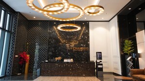 A modern reception area with a black marble wall, a reception desk, and three illuminated circular light fixtures. - Chambers PWTC By Unimax (Kuala Lumpur)