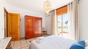 Une chambre à coucher avec un lit, une armoire en bois, une chaise, un bureau et une fenêtre avec des rideaux.