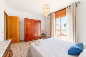 Een slaapkamer met een bed, een houten garderobe, een stoel, een bureau en een raam met gordijnen.