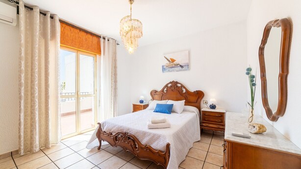 Une chambre à coucher avec un lit en bois, une table de chevet, une commode, un miroir et une fenêtre avec des rideaux.
