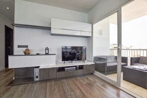 Een moderne woonkamer met een flatscreen-televisie, een inbouwmeubel en een schuifpui naar een balkon.