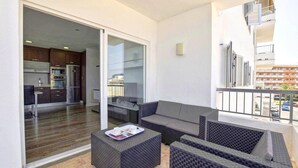 A balcony with wicker furniture, a sliding glass door leading to a kitchen, and a view of a building with balconies. - Apartment 'Son Baulo' with Sea View, Private Terrace and Wi-Fi (Can Picafort)