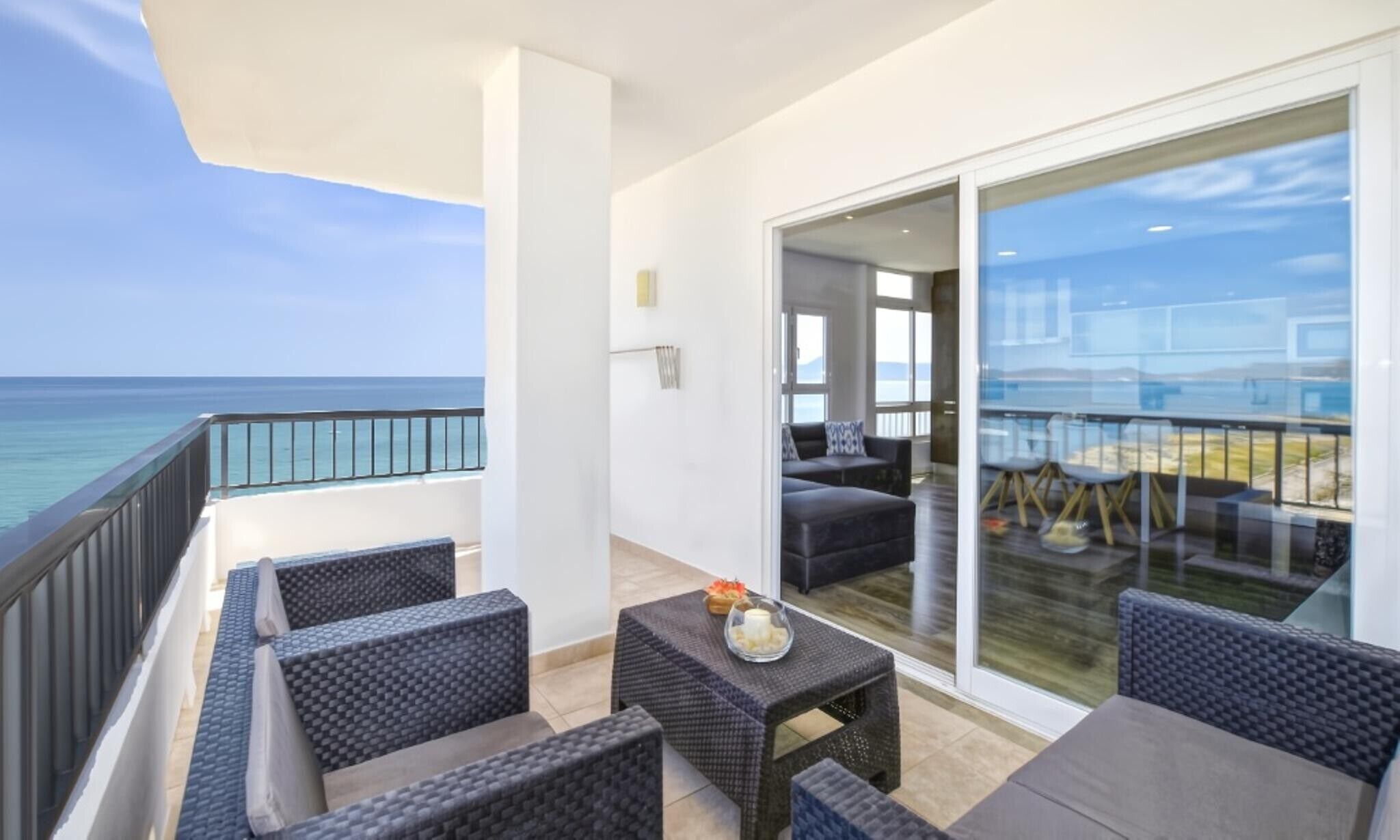 A balcony with outdoor furniture, a glass door leading to a room, and a view of the ocean.