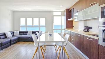 A modern kitchen with a dining area, large windows, and a view of the sea.