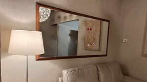 Un canapé beige avec une structure en bois, un lampadaire et un miroir fixé au mur qui reflète la pièce.