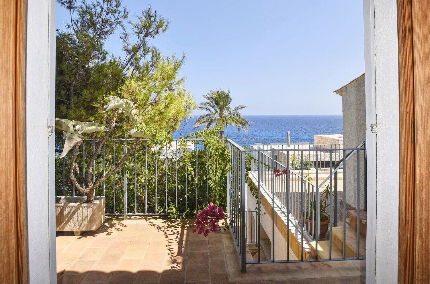 A balcony with a view of the sea, a metal railing, and potted plants.