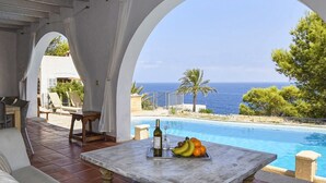 A poolside area with a table, chairs, and a view of the sea.