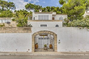 Un edificio blanco con un muro de piedra, una reja metálica y macetas con plantas.
