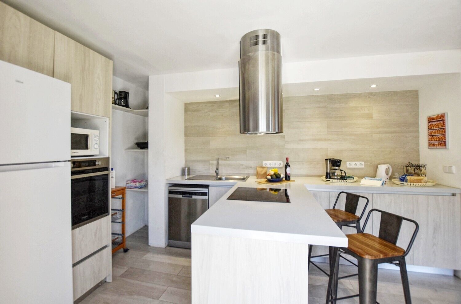 A modern kitchen with a central island, built-in appliances, and a stainless steel range hood.
