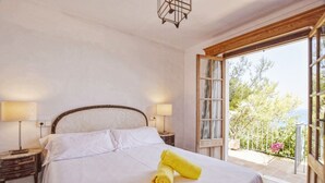 A bedroom with a bed, two bedside lamps, a window with a view of trees and a balcony.